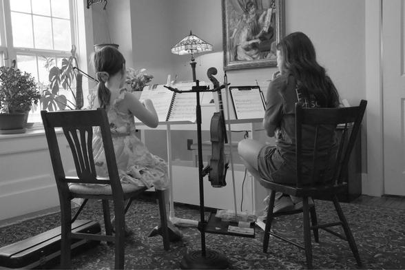 Two people sitting in chairs while one plays the violin.