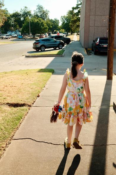 A girl walking down a sidewalk with a doll in one hand