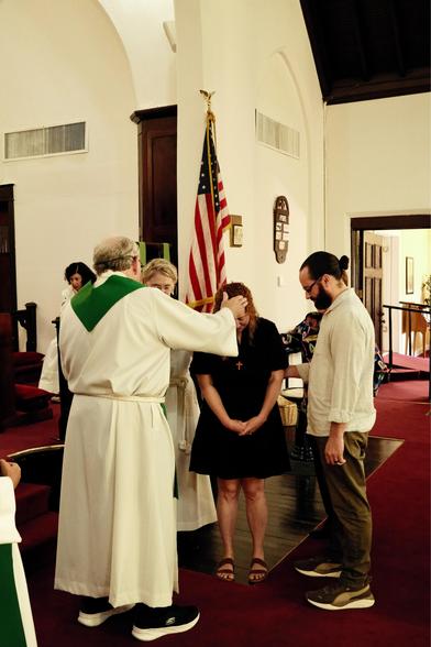 A priest laying hands on a woman in a church surrounded by people 
