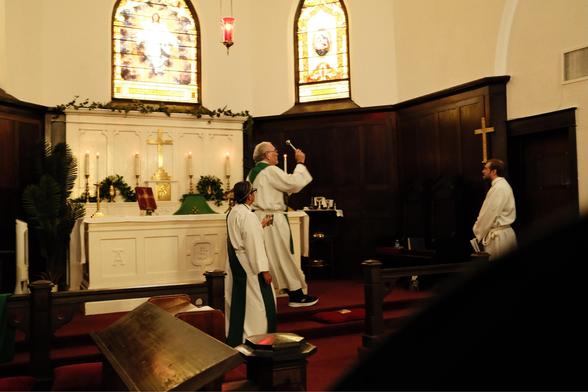 A priest scattering holy water against the wall of a church.
