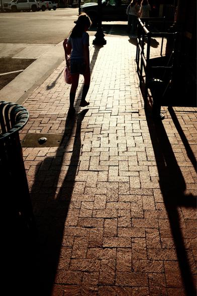Shadows of people walking down a brick sidewalk