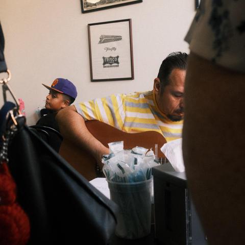 A man plays guitar in a coffee shop while a young boy listens to
