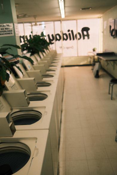 A line of washing machines with their lids open in a laundromat