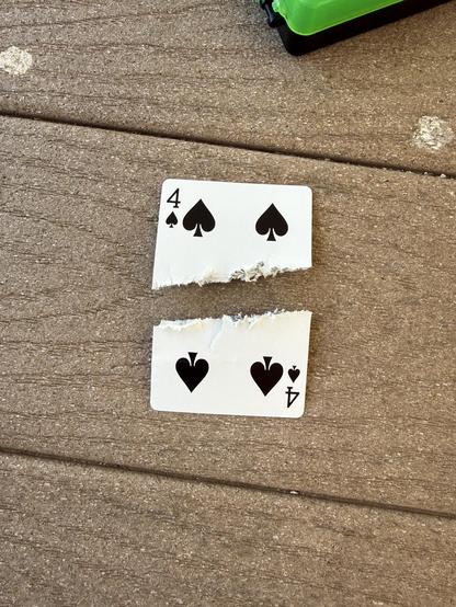 A 4 of spades card split laying on a table after being in half by a bullet.